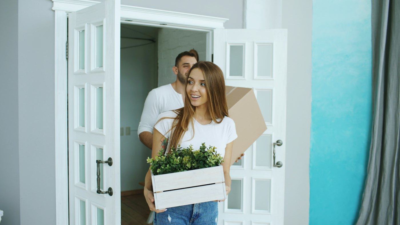 Pareja llegando a su nuevo hogar con una caja y plantas